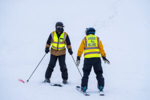A blind skier follows instruction from an instructor.