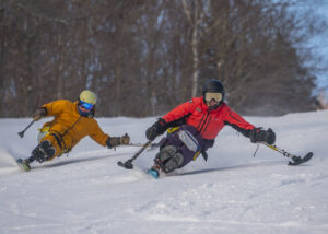 Two monoskiers mirror each other making arc turns down the ski hill.