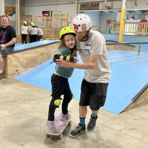 Young skateboarder getting the feel with his volunteer coach.