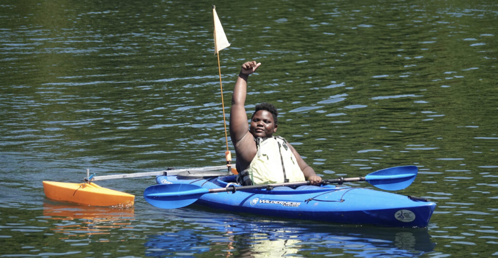 A young paddler is celebrating his success in the GMAS kayaking program by raising his arm and fist.